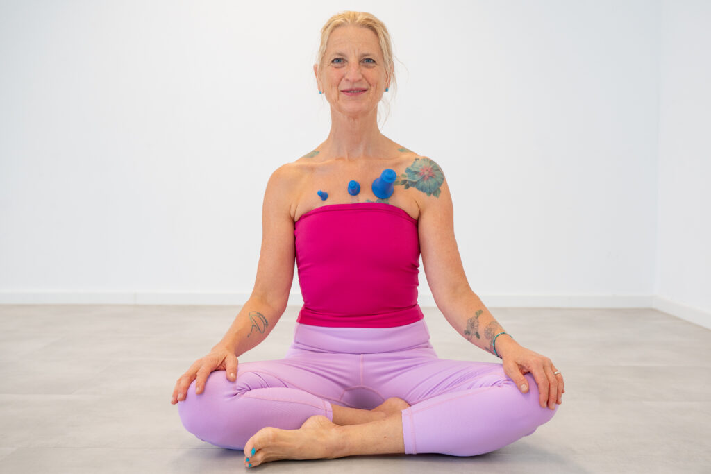 Miriam Wessels im Schneidersitz, pinkes Top, blaue Cupping-Becher auf dem Brustkorb